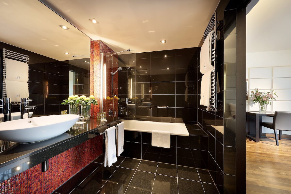 A modern bathroom with a large white sink, a glass-enclosed shower, and a black tiled floor.