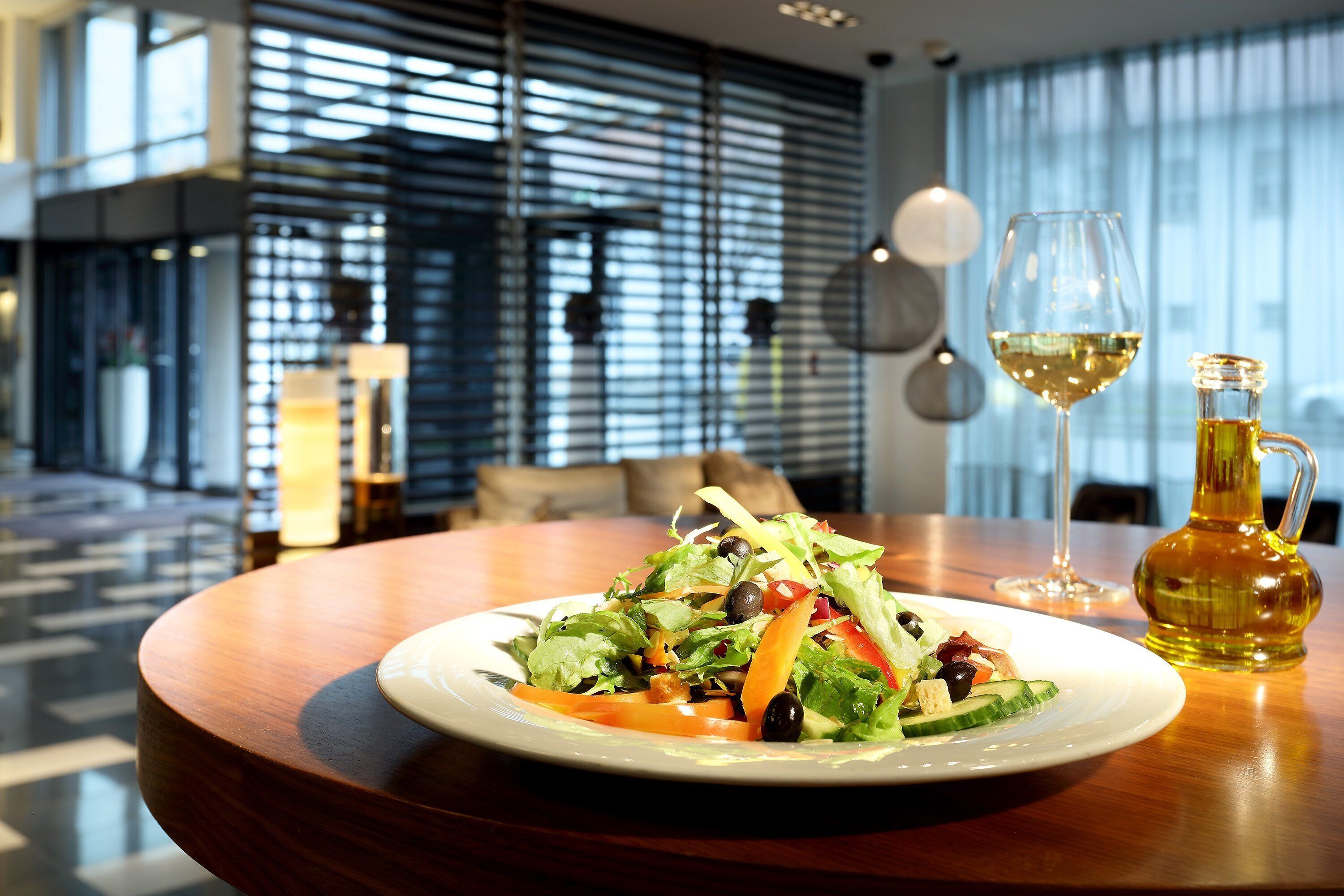 Een houten tafel met een salade, een glas witte wijn en een fles olijfolie.