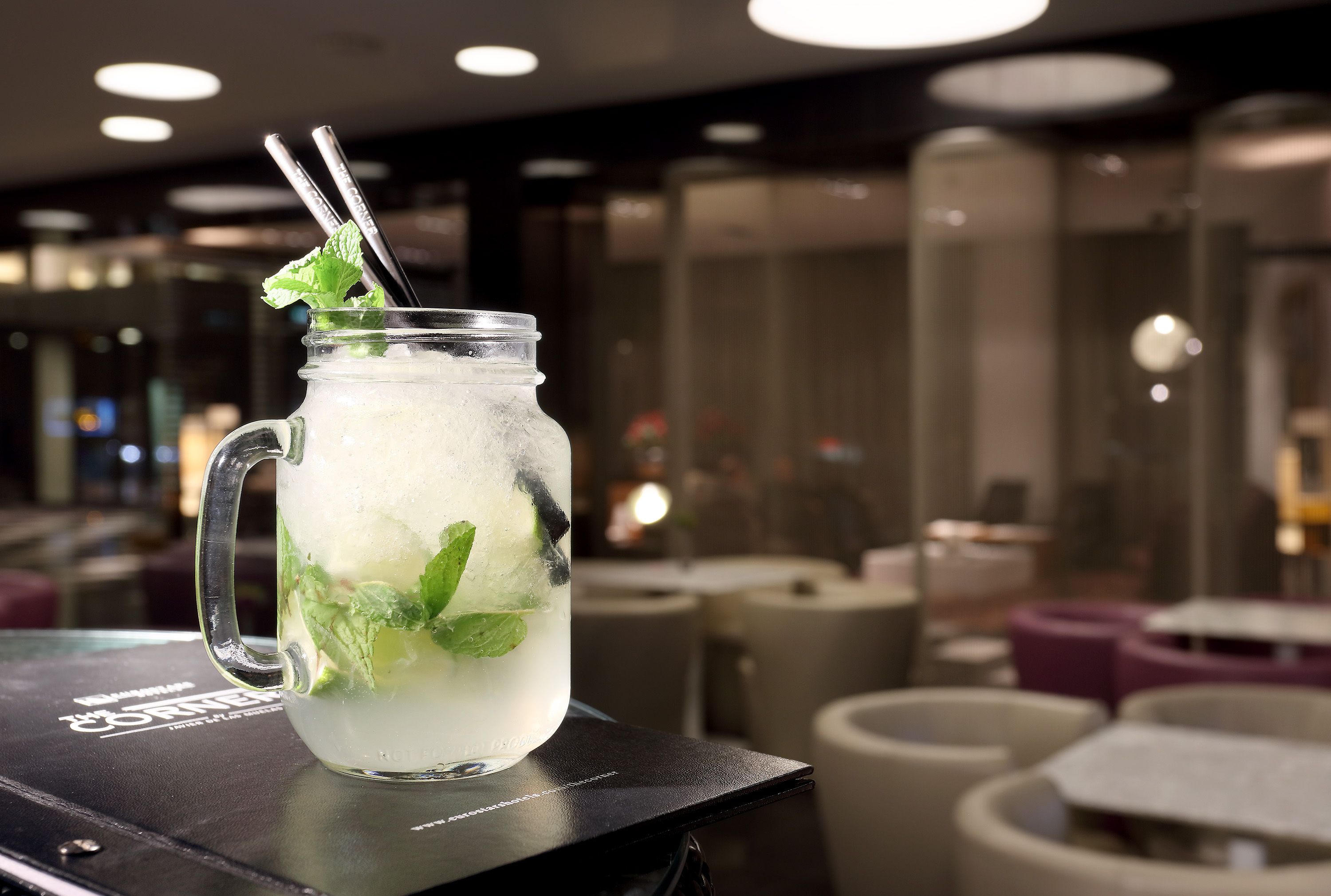 A clear glass mug with a straw and mint leaves on a bar counter in a modern interior.