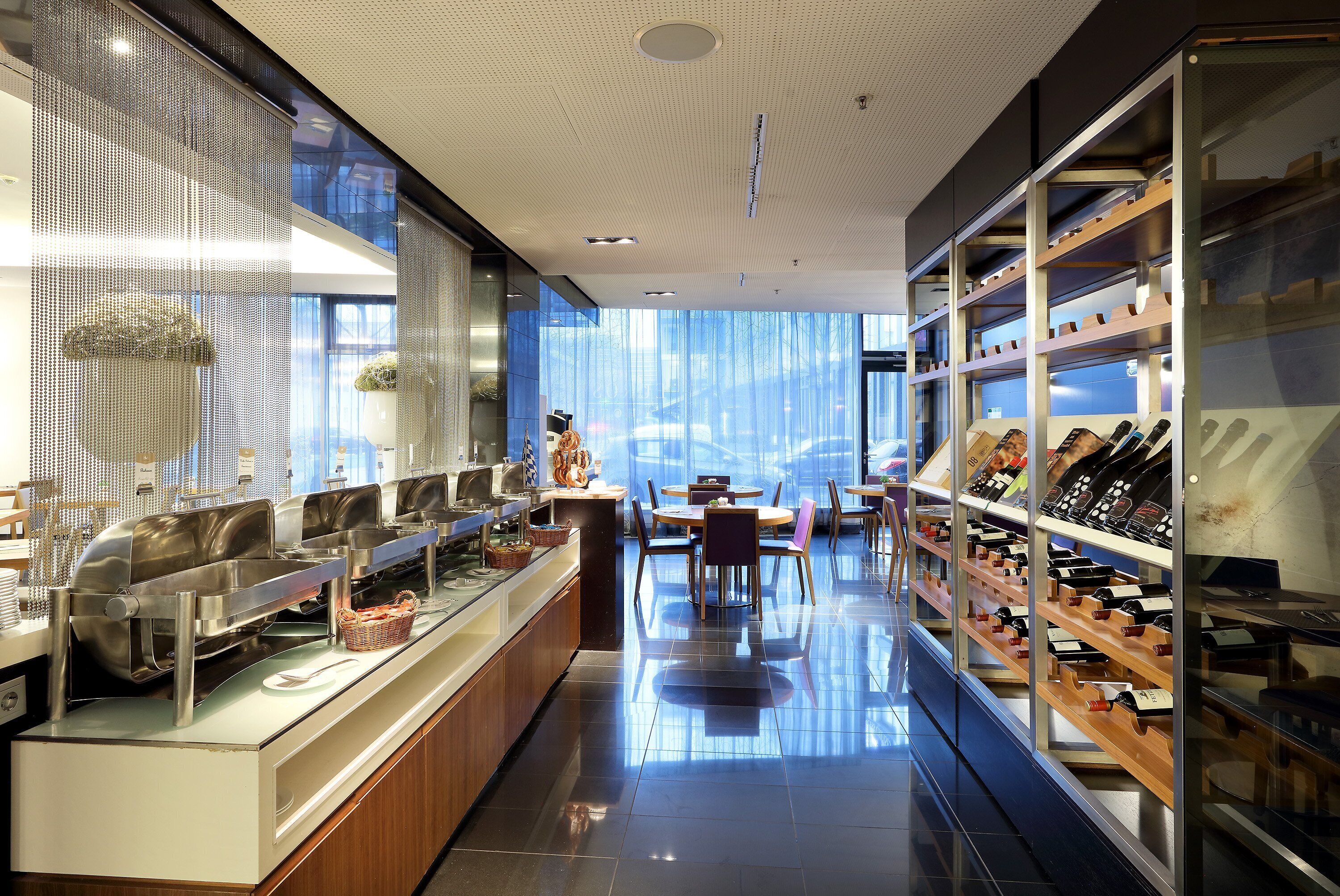 A modern hotel lobby with a buffet area, a seating area, and a wine display.