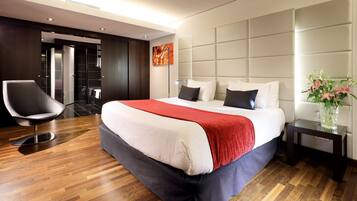 Habitación de hotel moderna con una cama grande, una silla, una mesita de noche y una obra de arte en la pared.