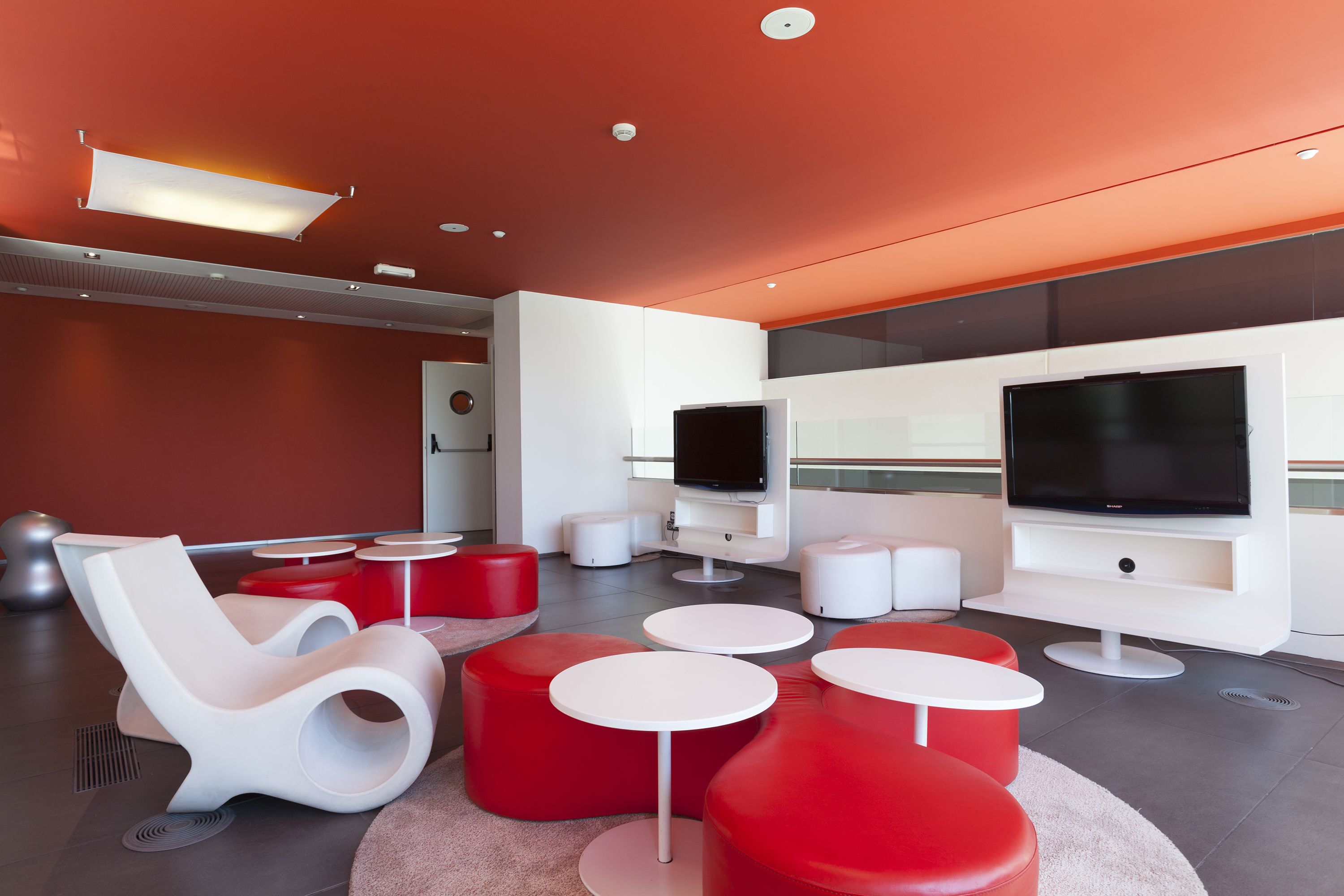 Un'area lounge moderna con televisione a schermo piatto, sedute rosse e bianche e un'ampia finestra.