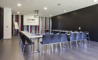 Una sala conferenze con un lungo tavolo e sedie, bottiglie d'acqua e un cartello con su scritto "axor hotels".