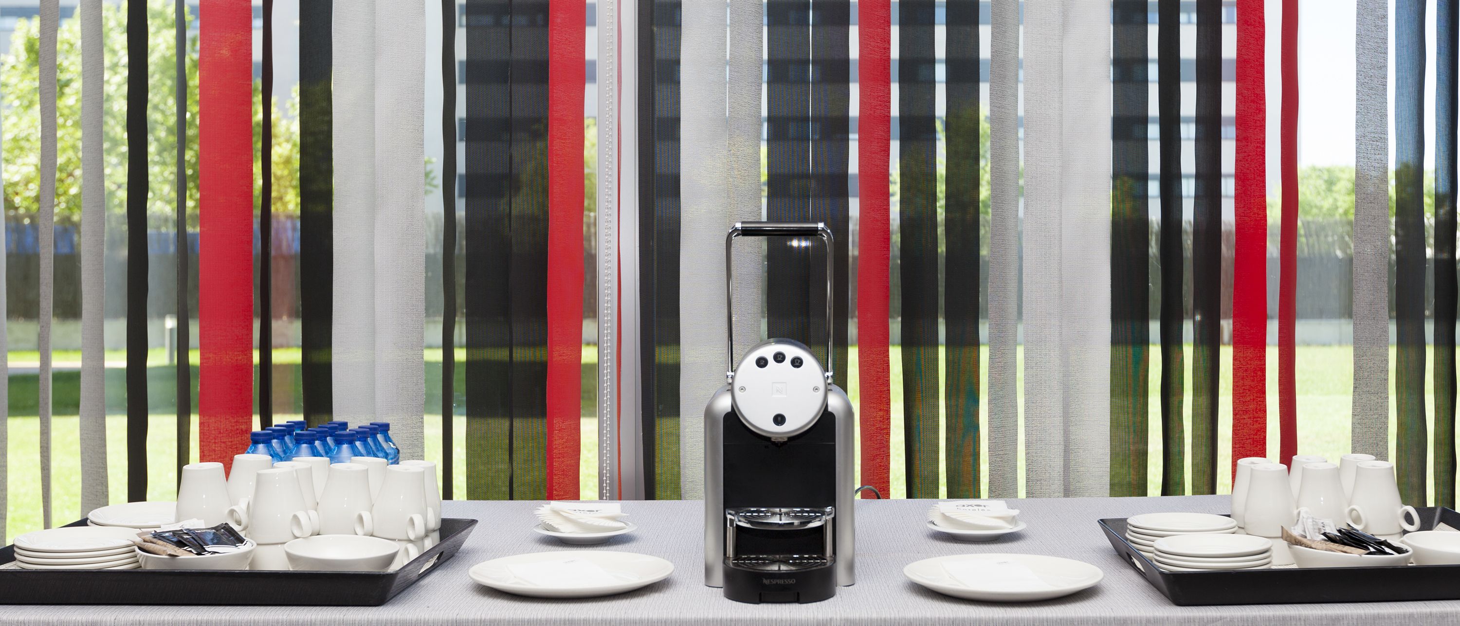 A coffee machine on a table with white cups and saucers, and a tray of blue water bottles.
