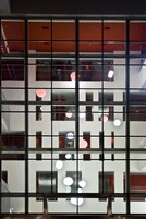 Ein mehrstöckiges Gebäude mit einer rasterförmigen Fassade, großen Fenstern und hängenden, kugelförmigen Lampen.