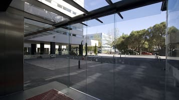 An outdoor area with a glass facade, a tiled floor, and a metal bench.