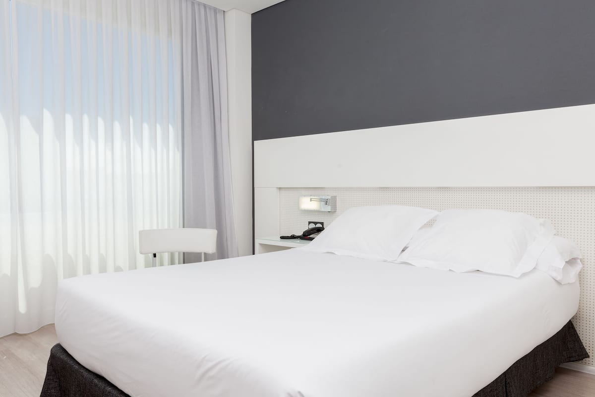 Moderni hotellihuone, jossa on suuri sänky, yöpöytä, lamppu ja seinälle asennettu puhelin.
