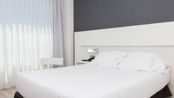 Ein modernes Hotelzimmer mit einem großen Bett, einem Nachttisch, einer Lampe und einem an der Wand befestigten Telefon.