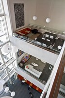Un interno moderno con ringhiera in vetro, un'area salotto con divano e poltrone, e un'area pranzo con tavolo e sedie.