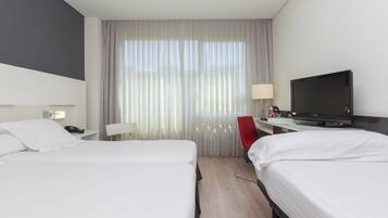 Camera d'albergo con due letti, una scrivania con televisore, una sedia rossa e una finestra con tende.