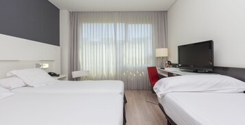 Camera d'albergo con due letti, una scrivania con televisore, una sedia rossa e una finestra con tende.