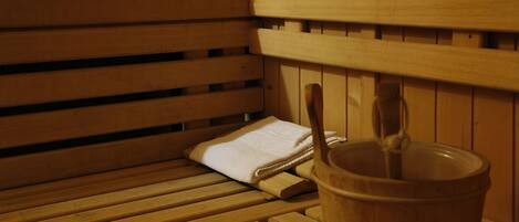 Un banco de sauna de madera con una toalla y un balde de madera.