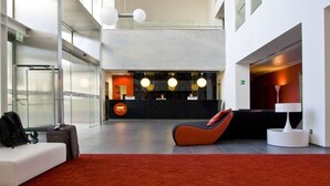 A modern lobby with a red carpet, seating areas, a reception desk, and a glass coffee table with a newspaper.