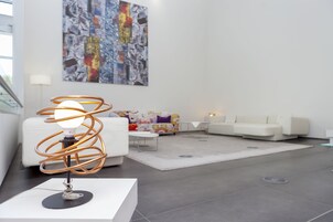 Ein modernes Wohnzimmer mit einer einzigartigen Kupfer-Spirallampe, einem weißen Sofa, einem farbenfrohen Sofa und einem großen, abstrakten Gemälde an der Wand.