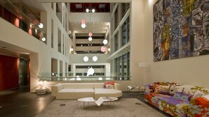 A spacious atrium with a modern interior, featuring a white sofa, a colorful sofa, and a white coffee table with magazines.