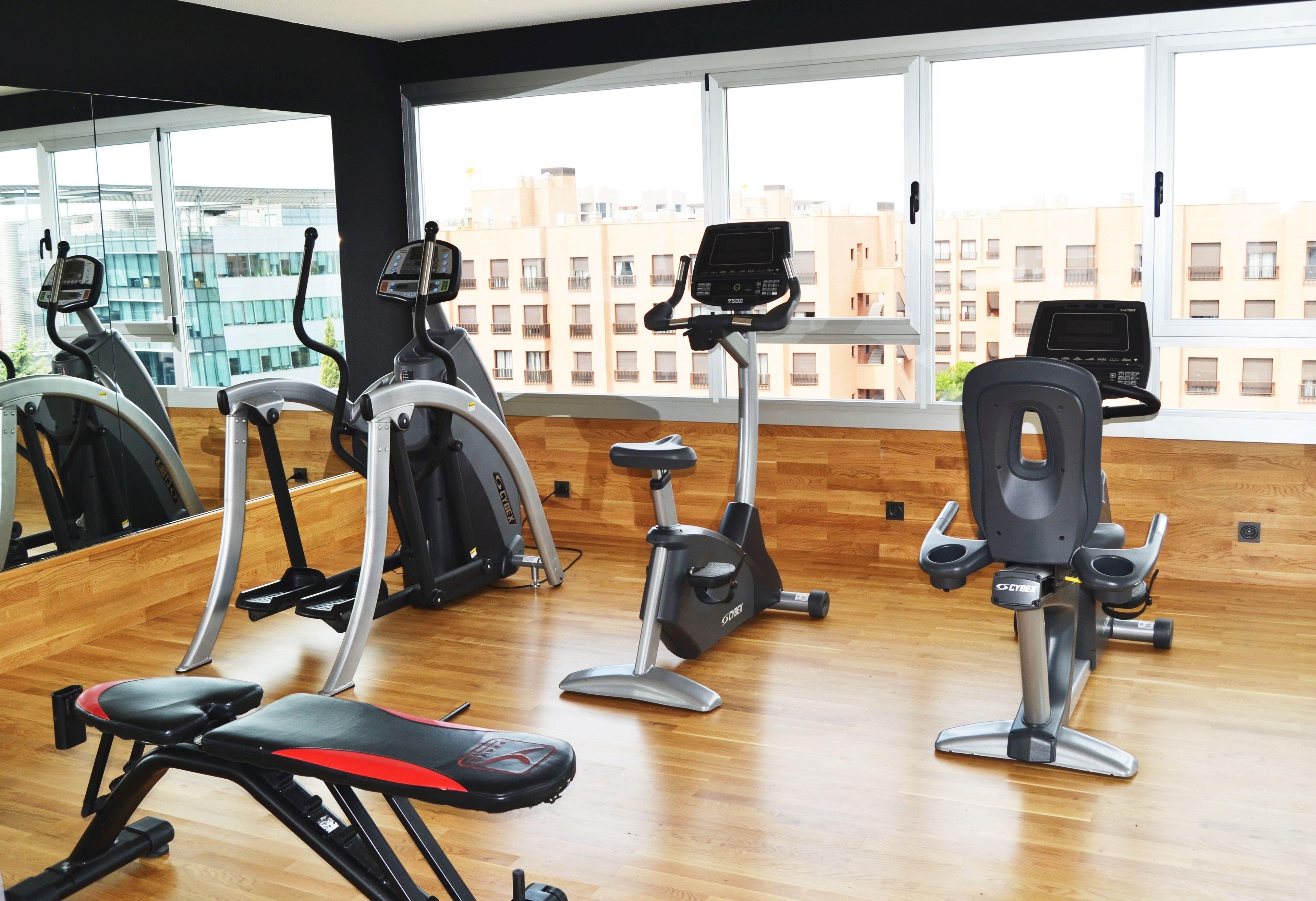 A gym with various exercise equipment, large windows, and a view of buildings outside.