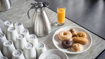 Un desayuno con cafetera, vaso de jugo y un plato de pasteles.