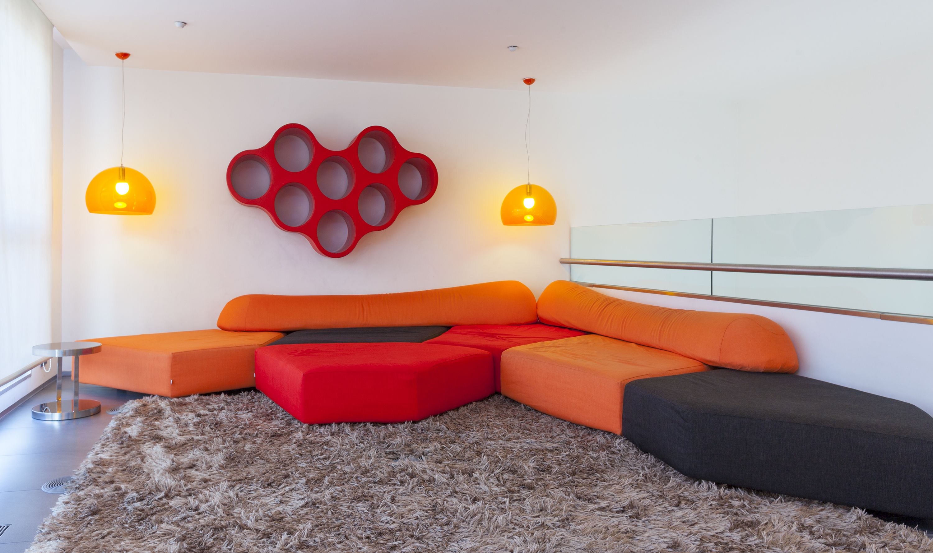 A modern living room with a sectional sofa in red and orange, a fluffy rug, and two pendant lights.