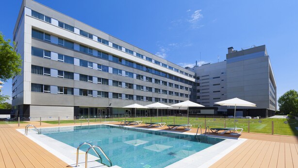 A modern hotel with a swimming pool, sun loungers, and umbrellas.