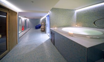 Ein Wellnessbereich mit einer großen Badewanne, einer hölzernen Sitzbank und einem Ablagebereich für Handtücher.