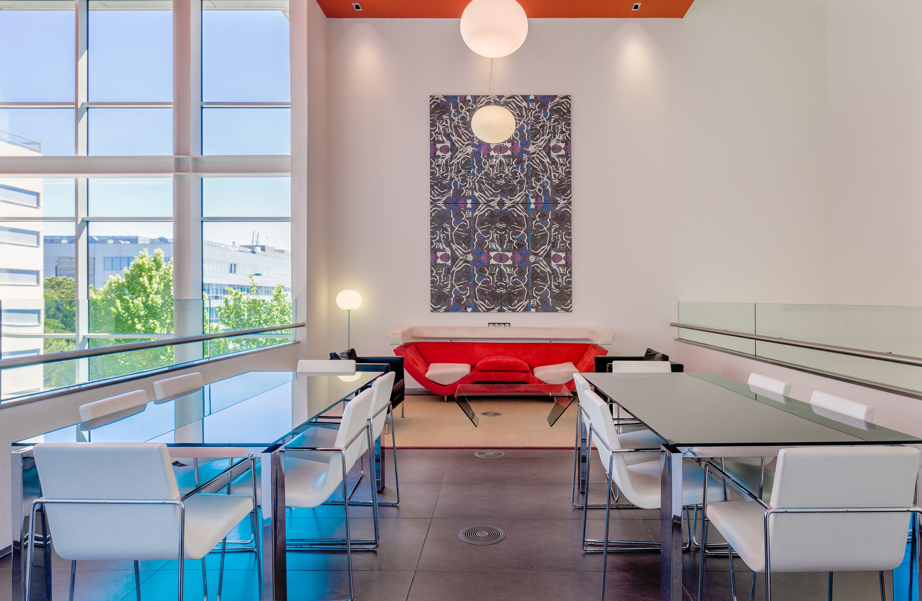 Una sala de reuniones moderna con mesas de vidrio, sillas blancas y un sofá rojo.