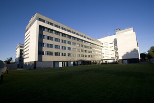 Un hotel moderno a più piani con tetto piatto e un ampio cortile lastricato di erba.