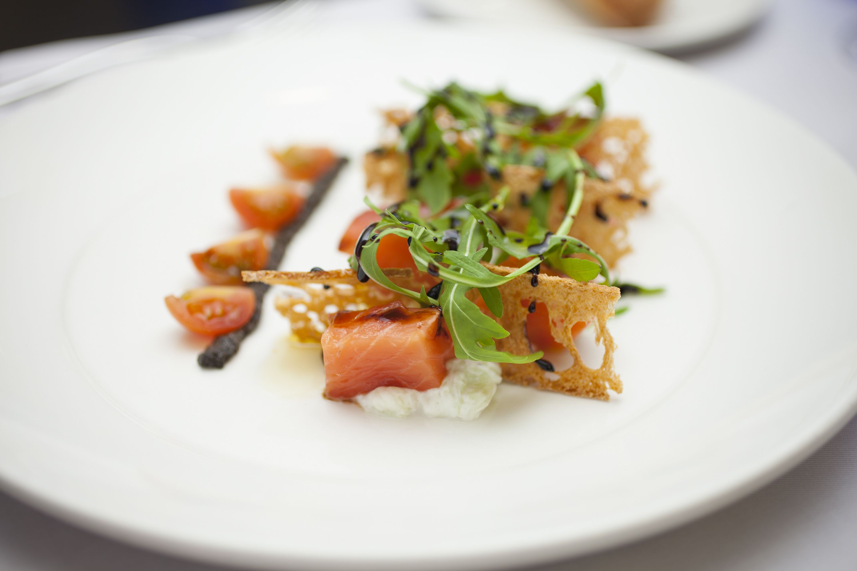 A white plate with a dish of smoked salmon, arugula, and cherry tomatoes.