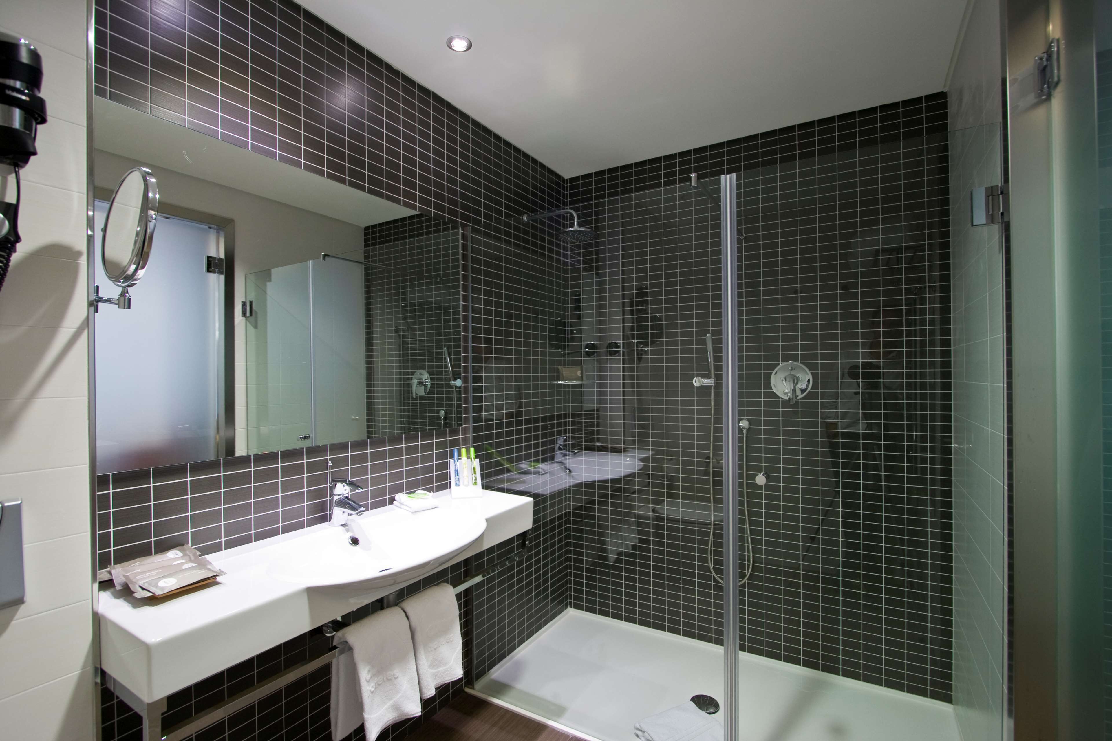 Un baño moderno con lavamanos, espejo y zona de ducha blancos.