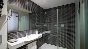 Un baño moderno con lavamanos, espejo y zona de ducha blancos.