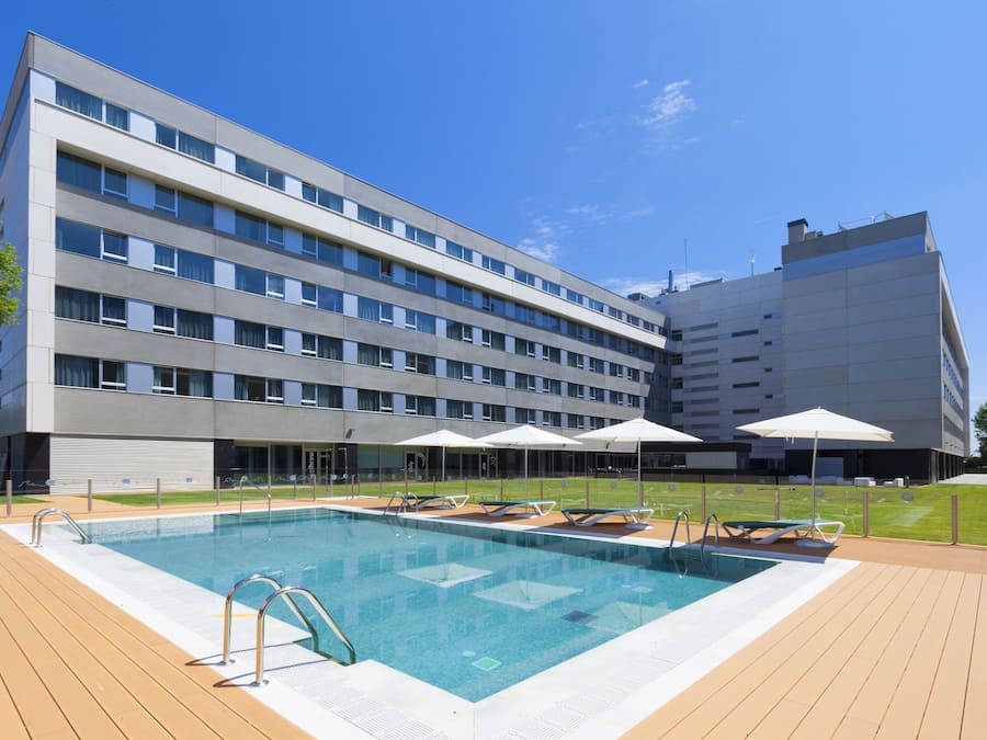 A modern hotel with a swimming pool, sun loungers, and umbrellas.