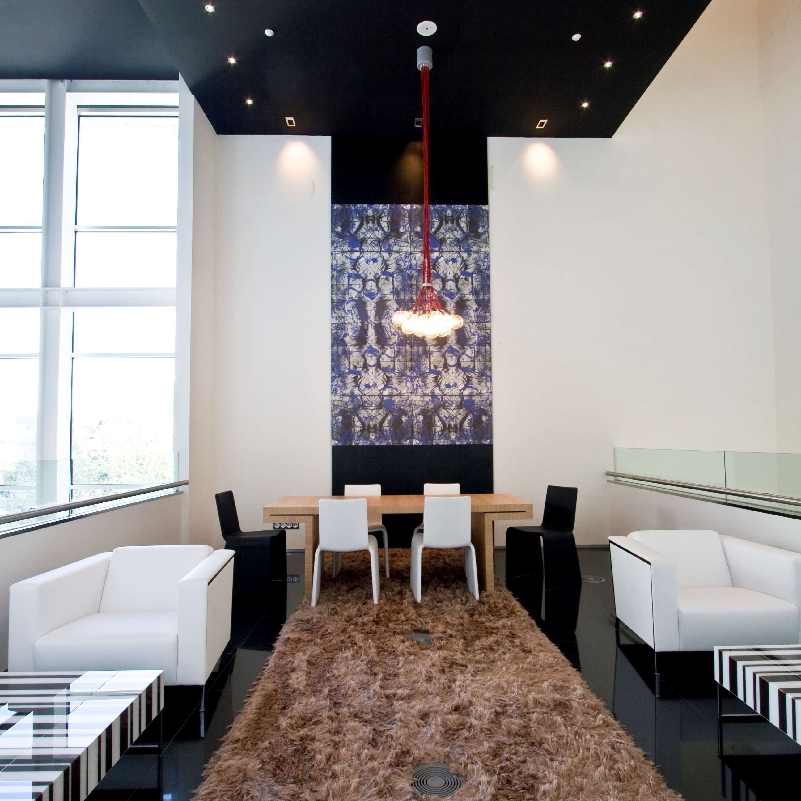 A modern conference room with a wooden table, white chairs, a black furry rug, and a unique blue and white abstract wall art piece.