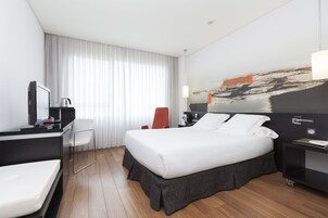 Una camera d'albergo moderna con un letto, una scrivania con una sedia, una televisione e un'ampia finestra con tende.