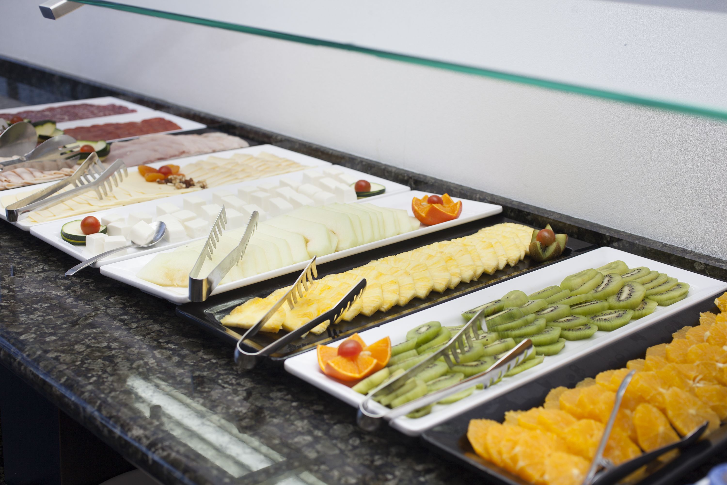 Buffet com diversas opções de comida, incluindo frutas, queijos e carnes.