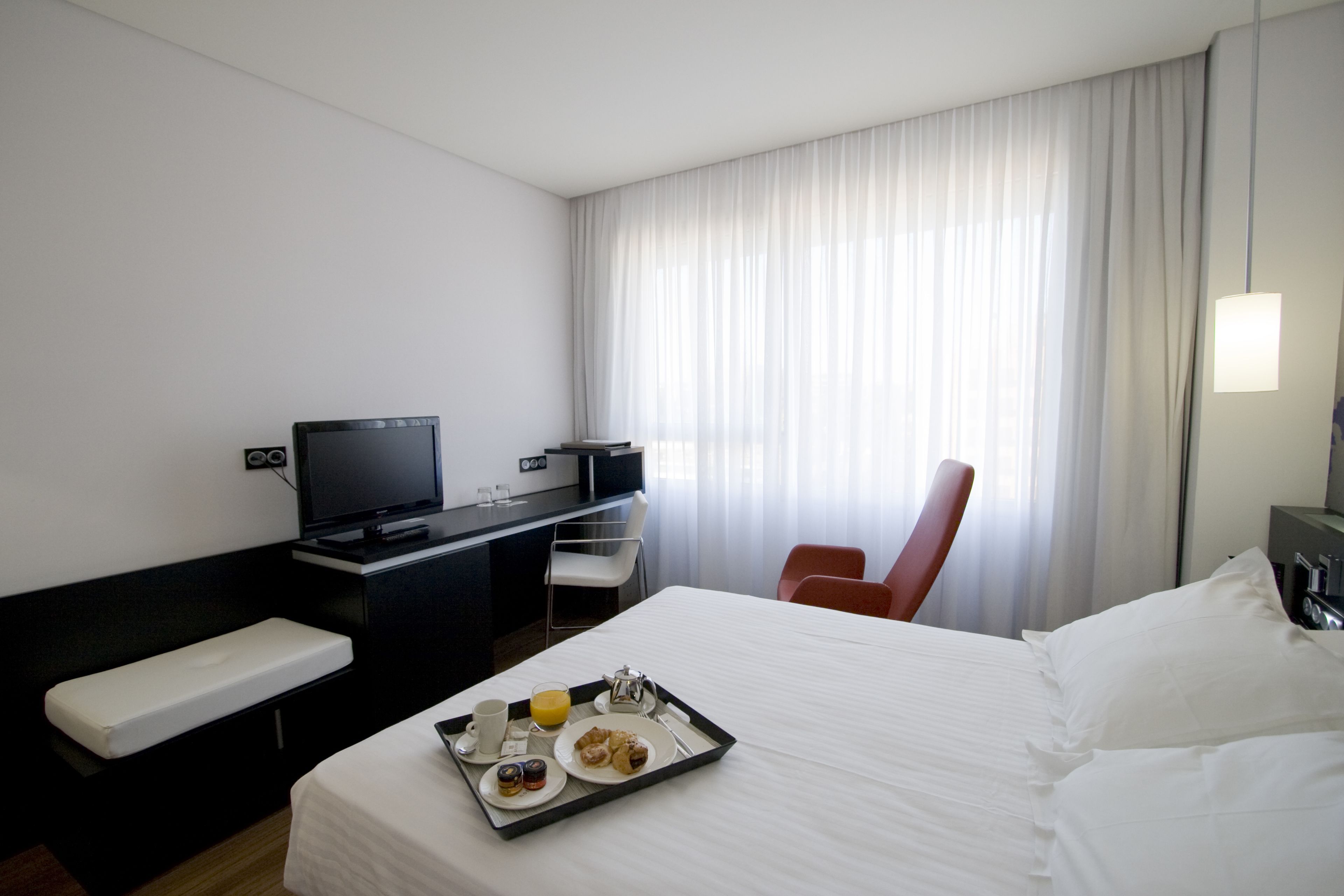 Una habitación de hotel con una cama, un escritorio con televisor, una silla y una bandeja con artículos para el desayuno.