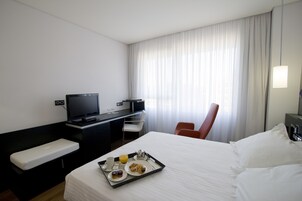 Ein Hotelzimmer mit Bett, Schreibtisch mit Fernseher, Stuhl und Tablett mit Frühstücksangeboten.