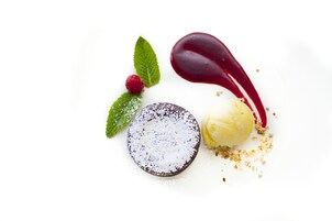 En dessert med chokoladebund, en kugle vanilleis og pynt bestående af en rød bær, mynteblade og flormelis.