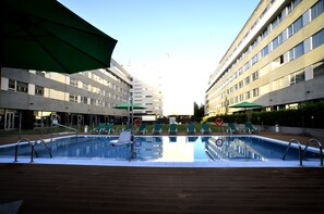 A swimming pool with lounge chairs and umbrellas, surrounded by modern buildings.
