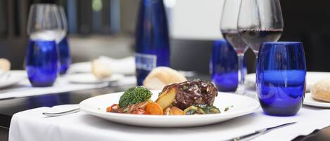 A dining table with a plate of food, wine glasses, and blue glassware.