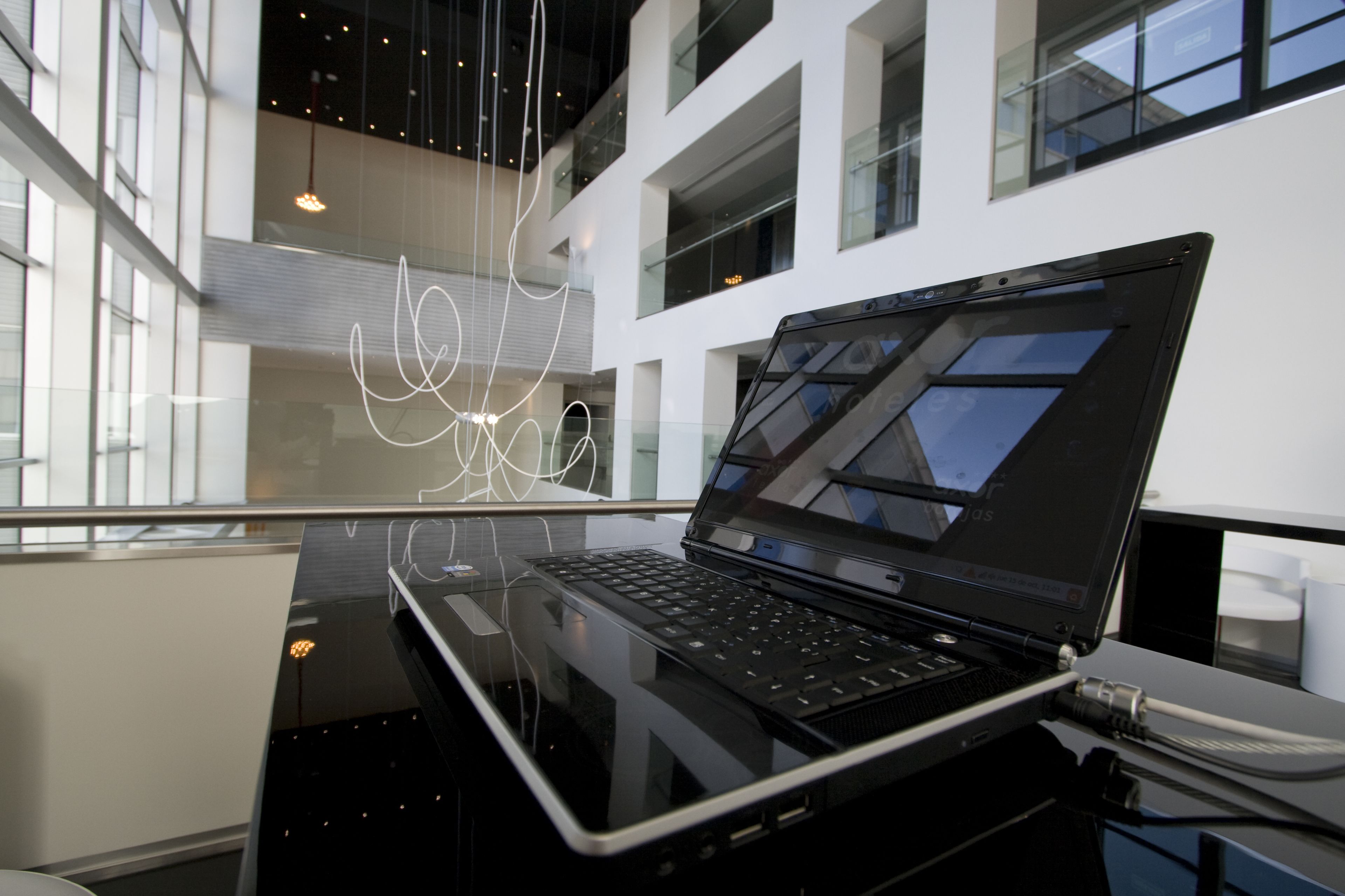 Un interior moderno con una laptop sobre una superficie reflectante, ventanas amplias y un diseño contemporáneo.