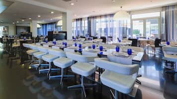 Un comedor amplio con varias mesas listas para el servicio, con sillas modernas y cubiertos de vidrio azul.