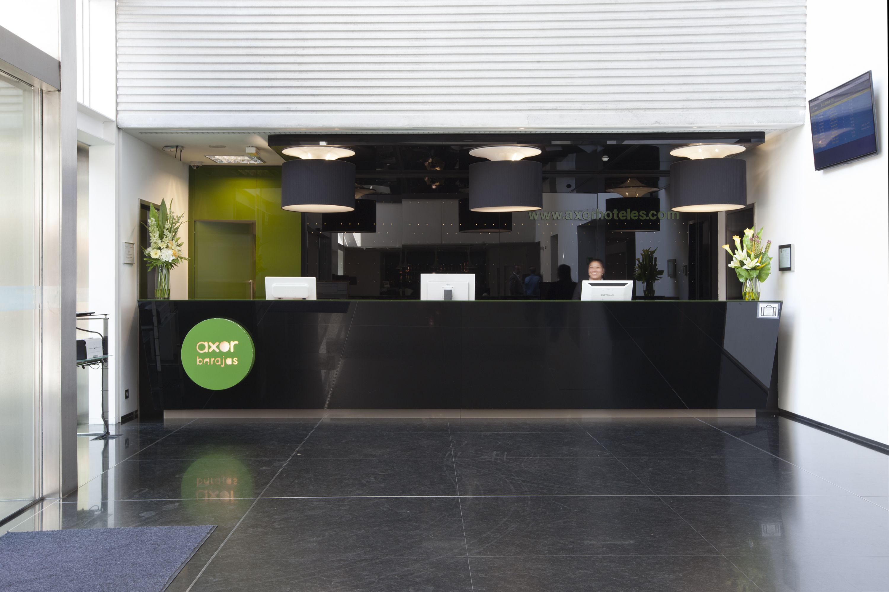 A reception desk with a black counter and green accent wall, two large pendant lights, and a digital screen.