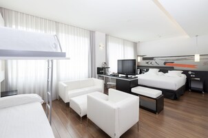 Una moderna camera d'albergo con un letto a castello, una scrivania con un computer, una televisione a schermo piatto, un divano e un comodino.