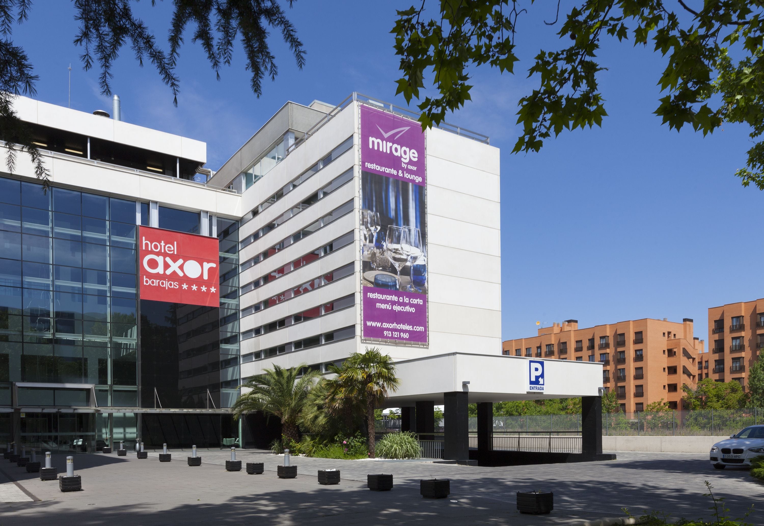 A hotel with a modern glass facade, a prominent 'hotel axor' sign, and a 'mirage' advertisement.