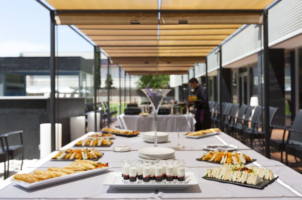 A long dining table with various food items and drinks, set up outdoors under a canopy.