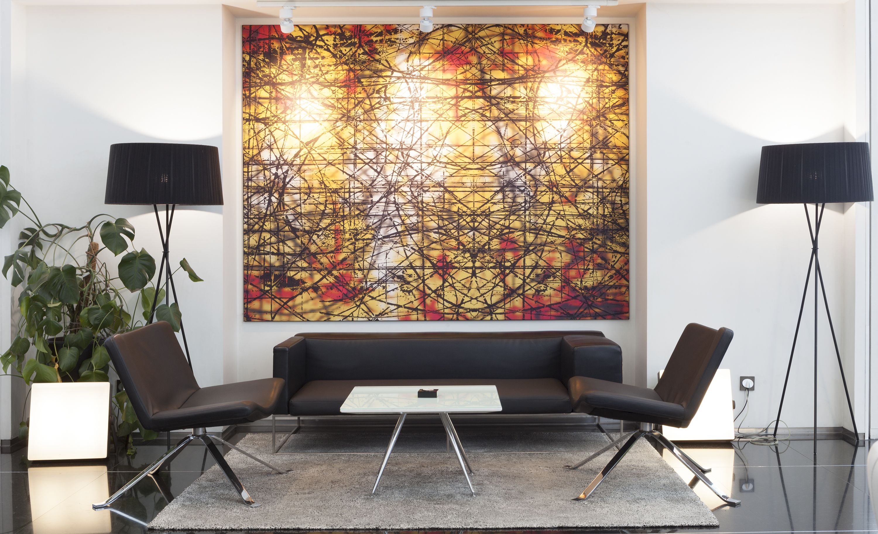 A modern living room with a black sofa, two black floor lamps, and a large abstract painting on the wall.