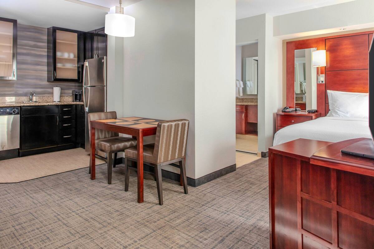A hotel room with a dining area, kitchenette, and a bed.