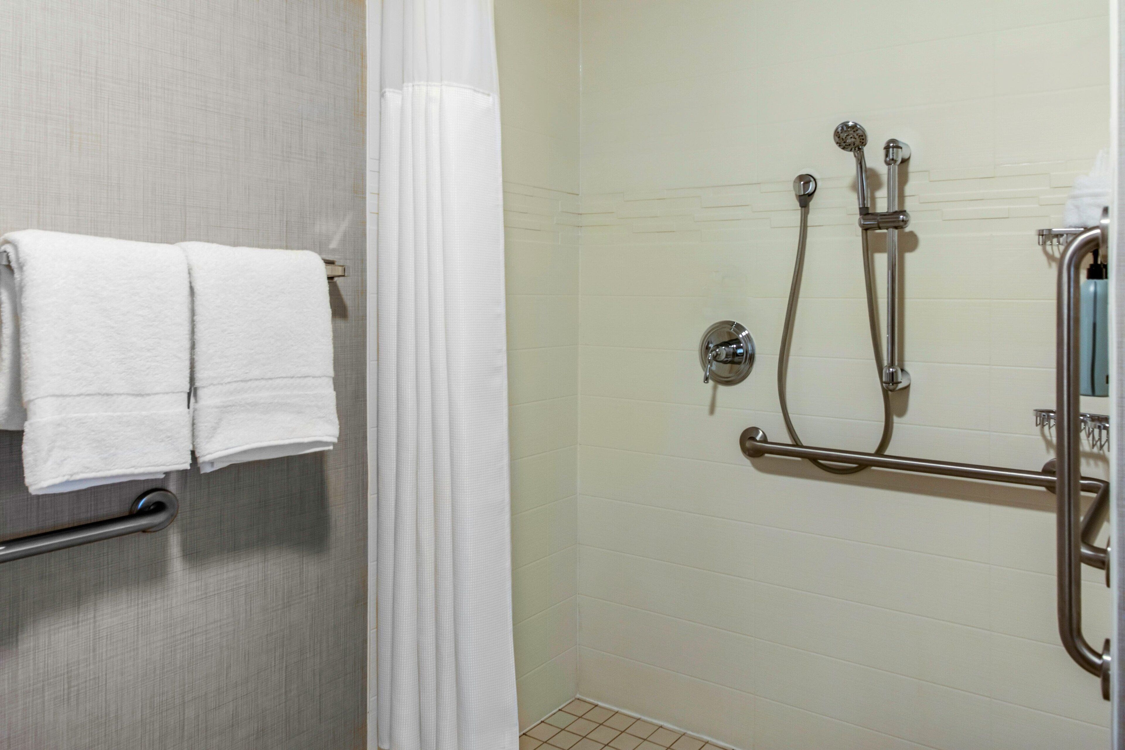 Un baño con ducha, un perchero con dos toallas y una puerta de cristal para la ducha.