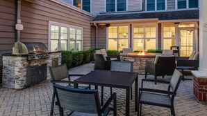 Une terrasse extérieure dotée d’une cheminée en pierre, d’un barbecue et de meubles en osier.