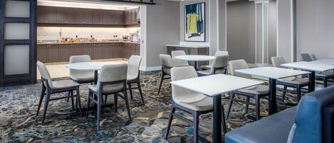 Un vestíbulo de hotel con una zona de cocina, varios arreglos de asientos y un cuadro abstracto grande en la pared.