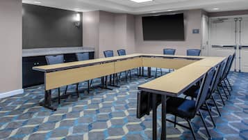 A conference room with a long table, chairs, a projector screen, and a carpeted floor.